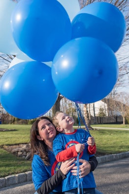 A boy with autism holding a few blue balloons and mother hugging him