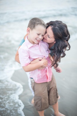 A boy with autism happy on a beach with his mother hugging him