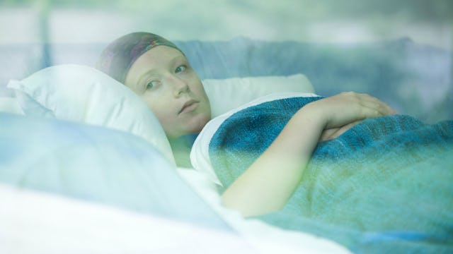 A young mom diagnosed with cancer lying down in a hospital bed, looking through the window.