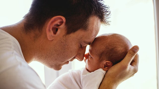A young father with short brown hair wearing a white shirt is holding his baby