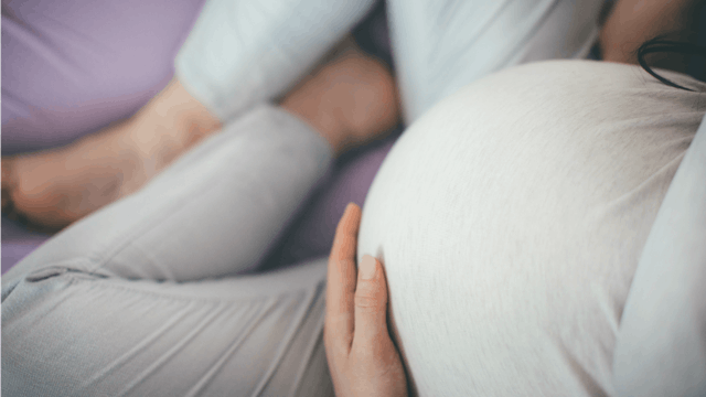 A not excited pregnant woman sitting on a bed