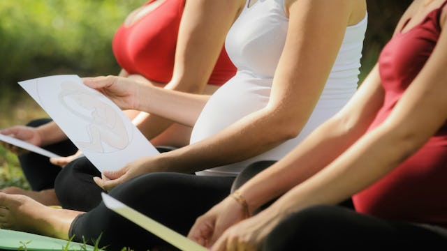 Three pregnant women sitting on yoga mats outside. 