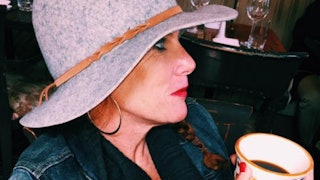 Leslie Blanchard wearing a blue denim jacket and a grey hat while holding a cup of coffee
