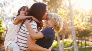 A stepmom carrying her daughter on her back while kissing and hugging her son.
