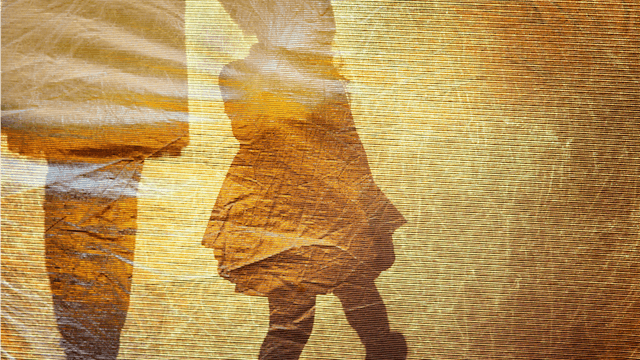 A shadow of daughter holding her mom’s hand on a yellow crumpled paper as a background