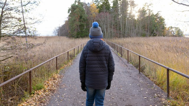 A boy walking down the road on an open field while wearing a winter jacket and a wool cap