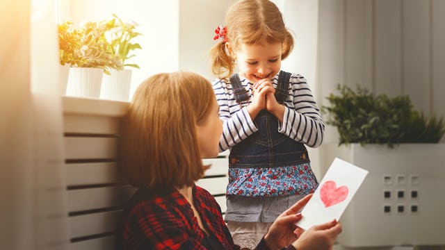 A brunette woman in a red and black sitting and holding a postcard from her daughter