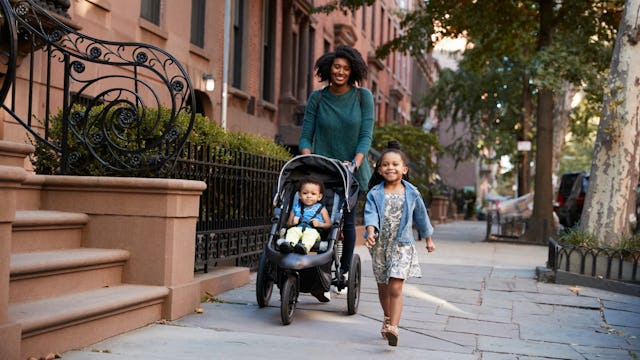A woman pushing a baby in a stroller and walking her toddler daughter