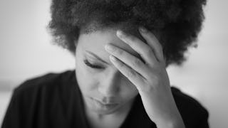 A woman looking down with a hand on her forehead suffering from Chronic Fatigue Syndrome 