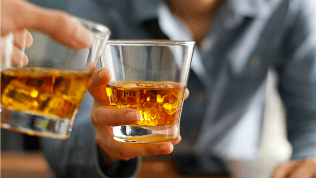 A man in a blue shirt holding a glass with liquor next to someone else's glass