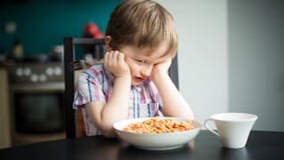 A boy in a striped short-sleeved shirt sitting at a brown table with a bowl of cereals in front of h...