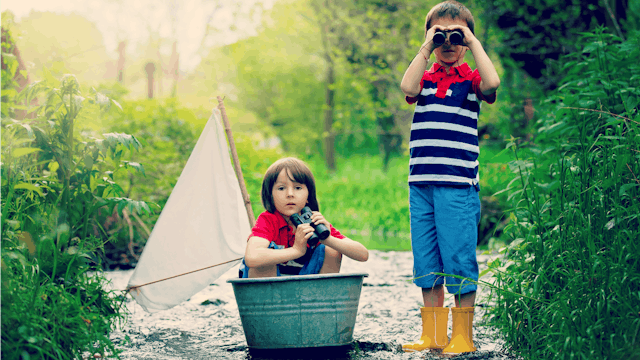 Two boys dressed similarly play in the water and peer through binoculars
