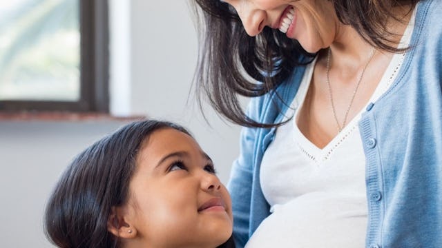 A pregnant mother and her daughter looking and smiling at each other 