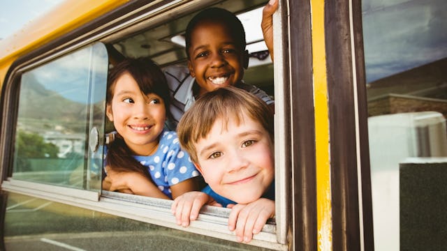 Three kids looking with a smile through an opened window of the school bus.