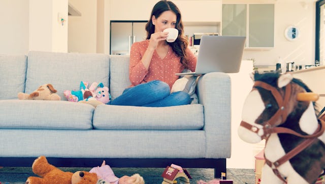A woman drinking a hot beverage peacefully on the couch while surrounded by a mess of toys