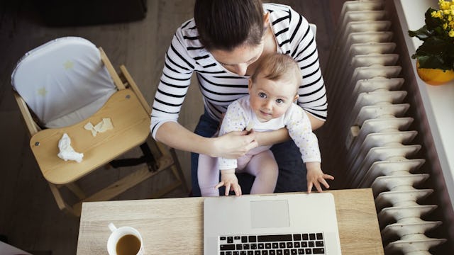 A mother working at home on her laptop while holding her baby on her lap