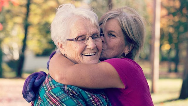 An older lady hugging and kissing her smiling mother in a park