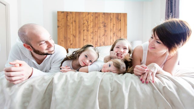 Parents in a bed with their three kids between them, smiling.