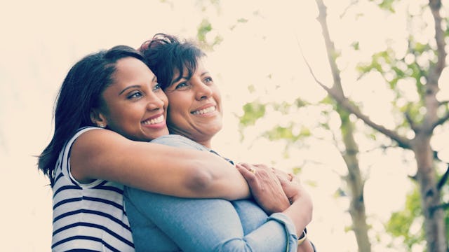 A grown woman wearing a white and black striped shirt and hugging her mom wearing a blue shirt from ...