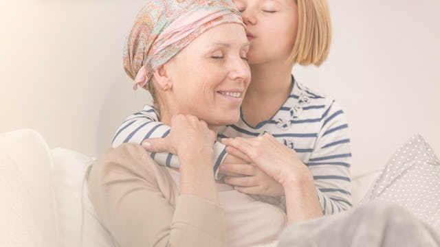 A daughter hugging her mother who is suffering from cancer while their sitting on a couch