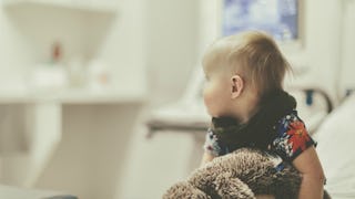 A blonde toddler diagnosed with a Pediatric Brain Tumor holding a plush toy in a hospital bed.