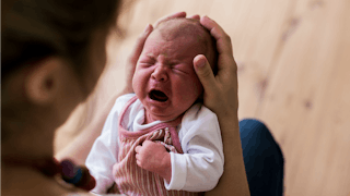 A baby hysterically crying in mother's hands and the mother thinking something is wrong
