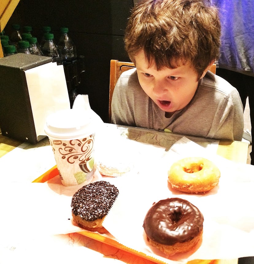 A boy looking at three different donuts next to a drink on a serving plate in 'The Donut Friar'