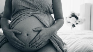 A woman pregnant with twins caressing her belly while sitting in black and white