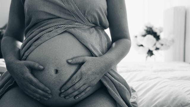 A woman pregnant with twins caressing her belly while sitting in black and white