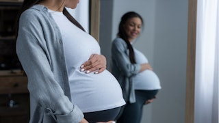 Young pregnant woman looking at herself in the mirror