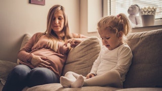 Pregnant mom sitting with her crying daughter on the couch