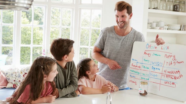 A father filling chore charts, with color-coded columns, with his children