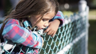 9-year-old girl standing leaned against a fence 