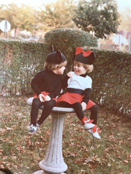 Two toddlers sitting in a garden dressed as Mickey and Minnie Mouse. 