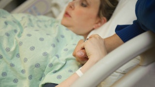 A pregnant woman is holding her daughter's hand while she is lying on the hospital bed 