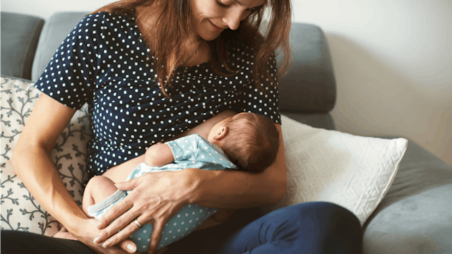 A brunette woman breastfeeding her baby while sitting on the sofa