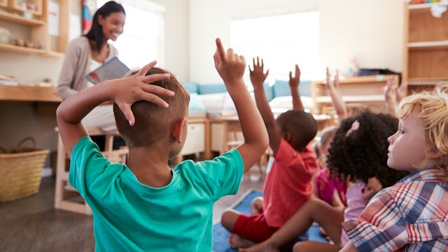 A group of kids sitting sitting on the floor with their hands up in a classroom