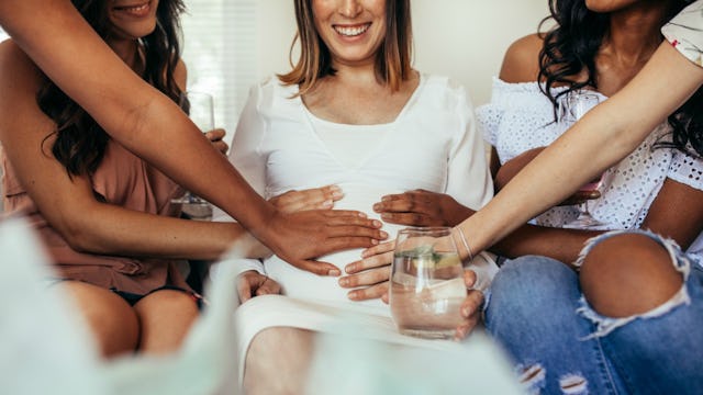 Female friends holding their hands on a new mom's belly