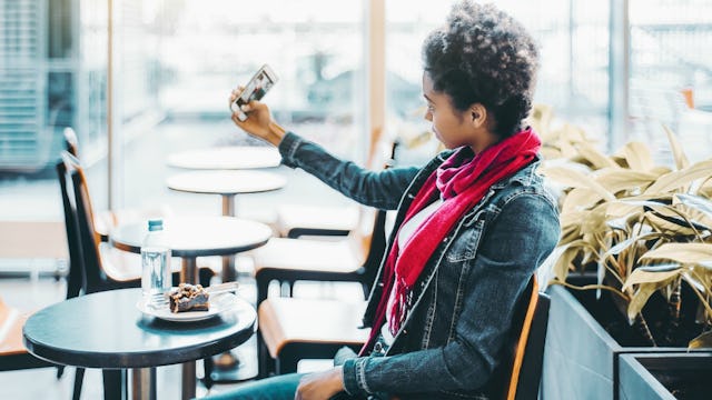 A woman in her mid-30s sitting in a café, taking a selfie