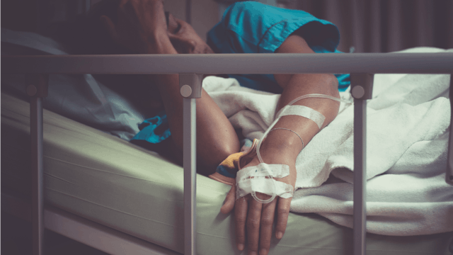 A woman in a blue hospital gown lying in a hospital bed after her recurrent miscarriage