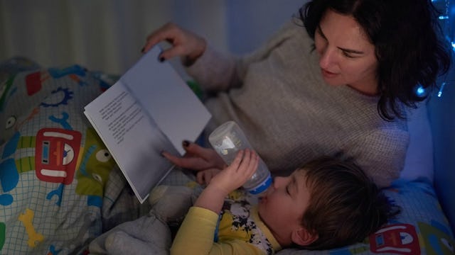 A mother reading a bedtime story to her son, who's drinking milk from a bottle