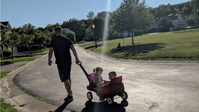 A father pulling a toy wagon with his son and daughter in it