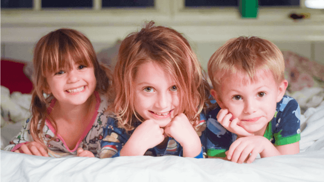 Three children lying on the bed smiling and looking straight into the camera