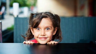 A five-year-old smiling, with her eyes widely open at the table