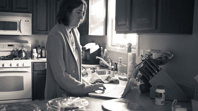 A black and white photograph of a mom looking at her laptop in the kitchen, feeling like a 'mom mart...