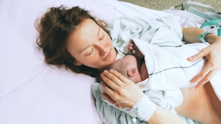 A woman lying in the hospital bed with her newborn baby in her arms right after giving birth