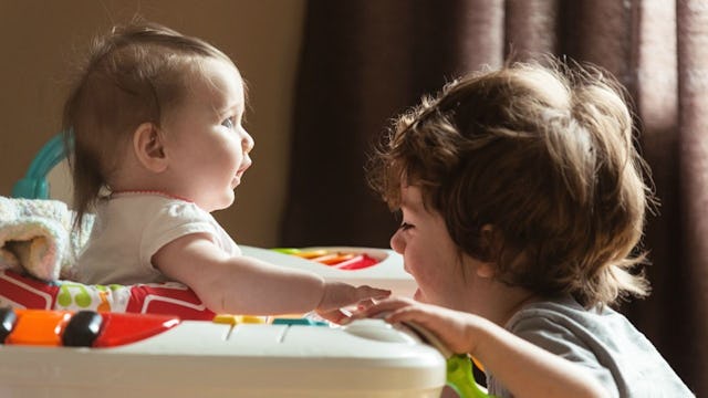 Two kids with a two-year age difference, one is in a baby walker and the other is leaning onto it