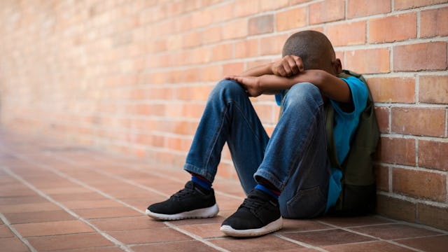 A child wearing blue denim jeans, a blue shirt, and black shoes sitting on the orange tiled floor wi...