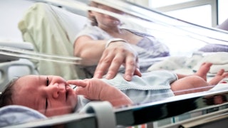 A mother lying down next to her baby in the neonatal intensive care unit NICU