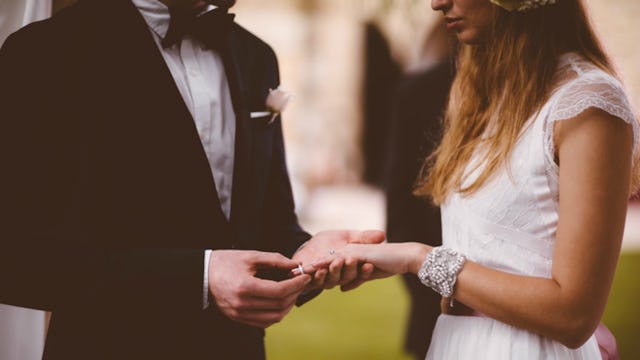 A groom in a black tuxedo putting a wedding ring on a bride's finger